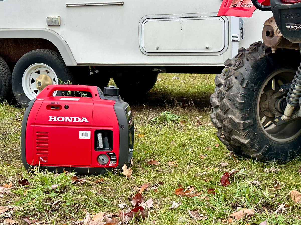 A Honda generator next to a camper and ATV at a camp site