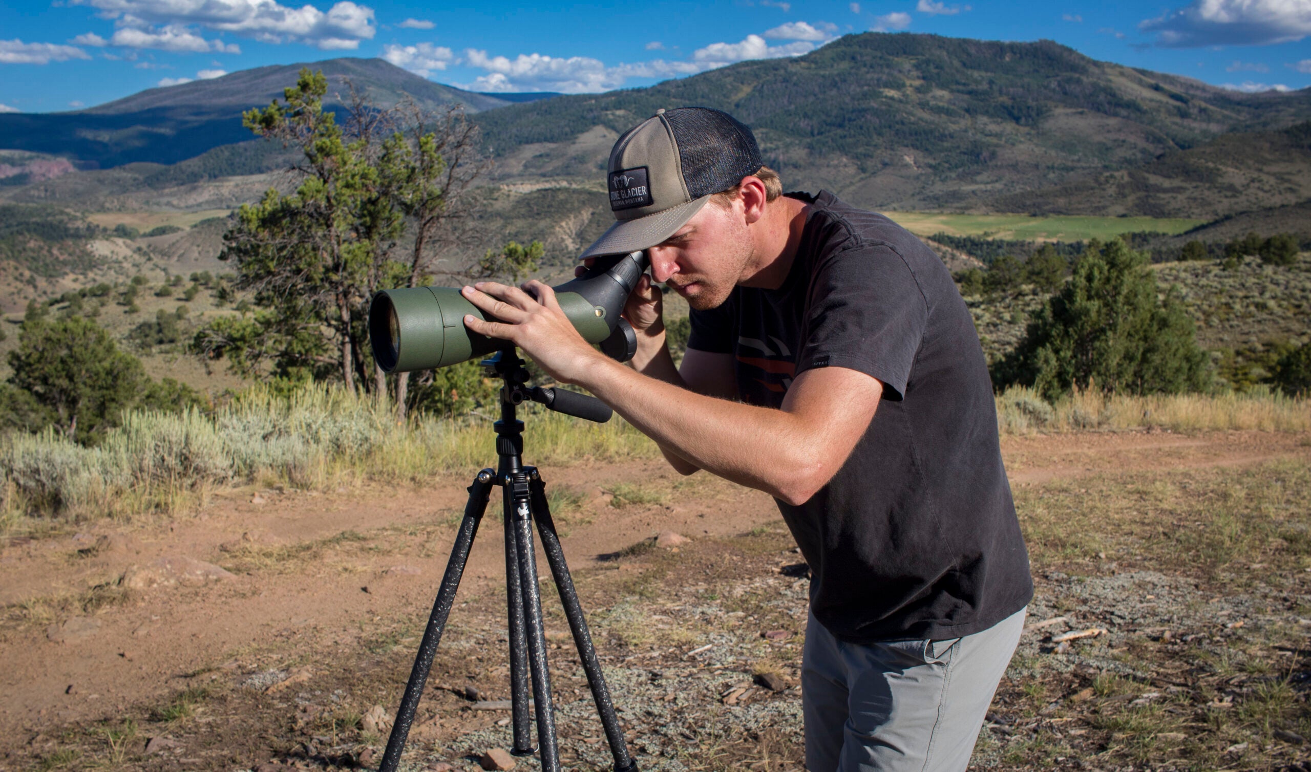 man looking through spotting scope in the mountains