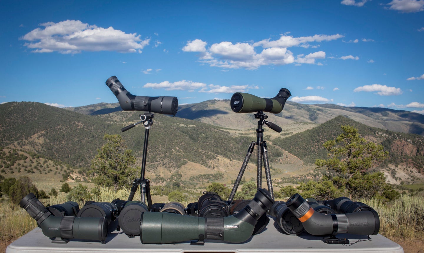 A table of spotting scopes with two spotting scope on tripods and mountains in the background