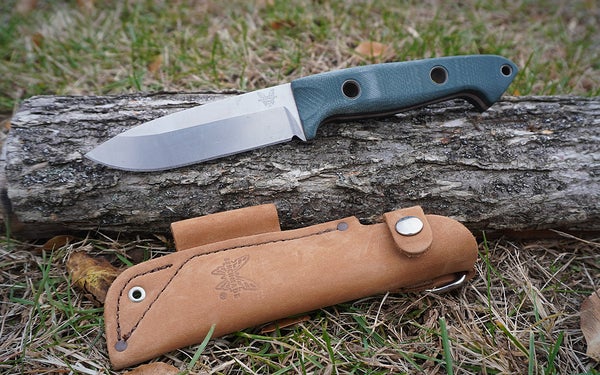 The blue and silver Benchmade Bushcrafter knife and brown sheath on a log.