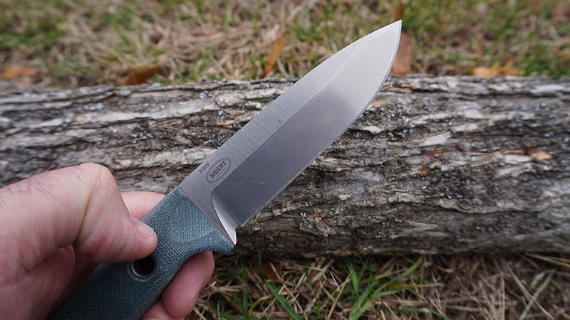 The blue G10 handle and silver blade of the Benchmade Bushcrafter knife above a gray log. 