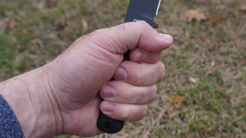 A close-up of a hand holding a Ka-Bar fixed blade knife above a grassy lawn. 