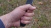A close-up of a hand holding a Ka-Bar fixed blade knife above a grassy lawn. 