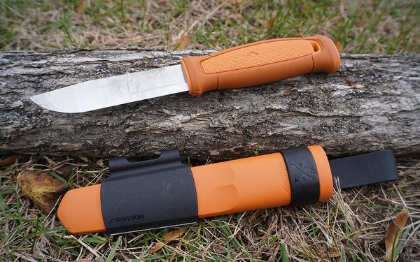 The tan and silver Morakniv Kansbol knife on a log on a lawn.
