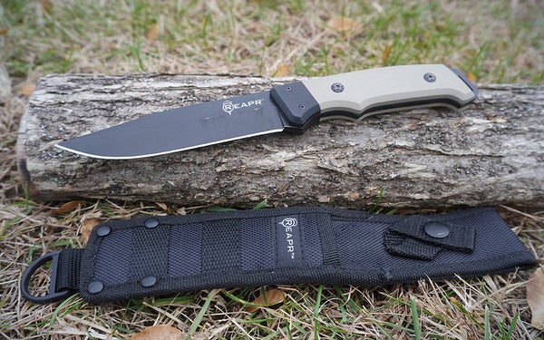 The black and tan Reapr Brigade knife with a black sheath on a cut log.