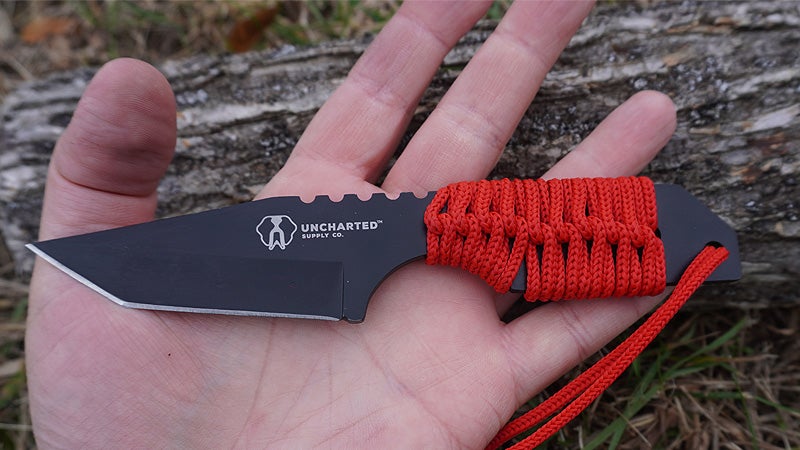 The red and black Uncharted Supply Co Prospector knife on a palm to show the size. 