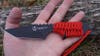 The red and black Uncharted Supply Co Prospector knife on a palm to show the size. 