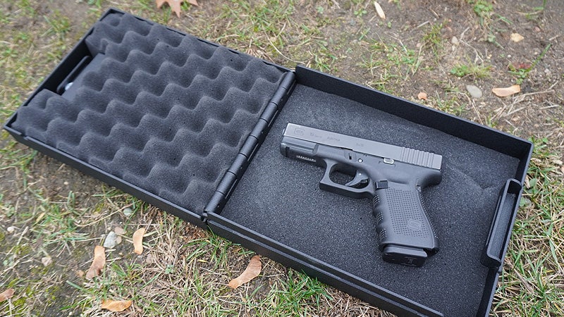 A black pistol box open showing a Glock 19 inside while sitting on a grassy lawn. 
