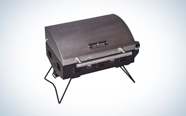 A silver and black Camp Chef portable BBQ grill on a black and white gradient background.