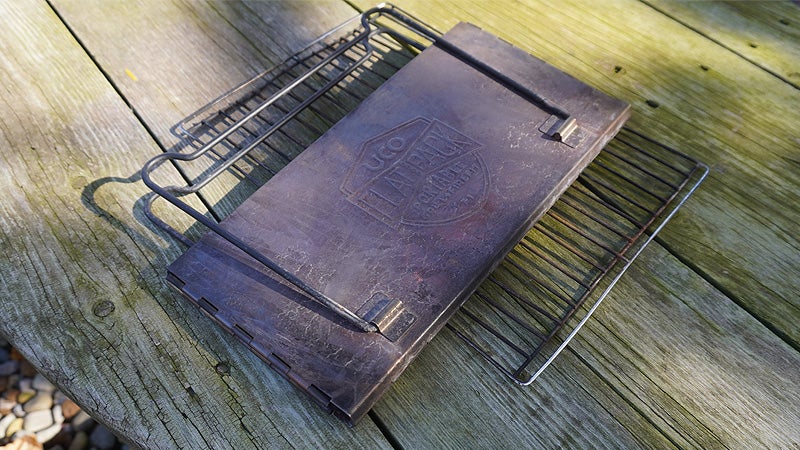 The UCO flatpack grill folded flat with the grill on a wooden picnic table. 