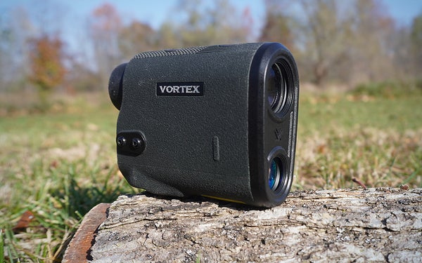 A green and black Vortex Diamondback HD 2000 rangefinder on a log on a grassy lawn.