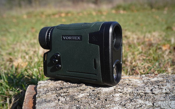 A green and black Vortex Viper HD 3000 rangefinder sitting on a log with the lens pointed to the right.