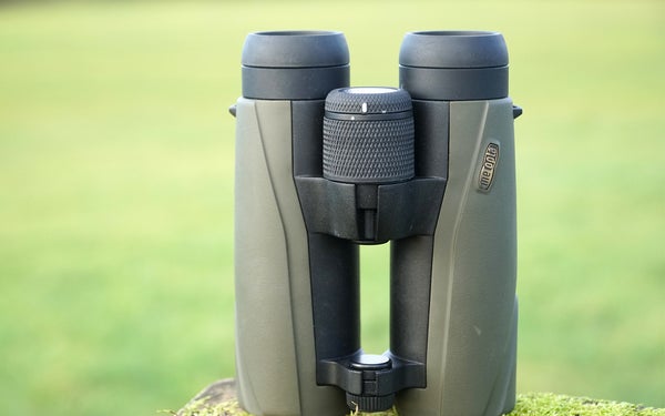 Meopta Meo Pro Air 10x42 binocular sitting on mossy wood with green field in background