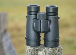 Nikon Monarch M7 10x42 binocular sitting on a fence post with a field in background.