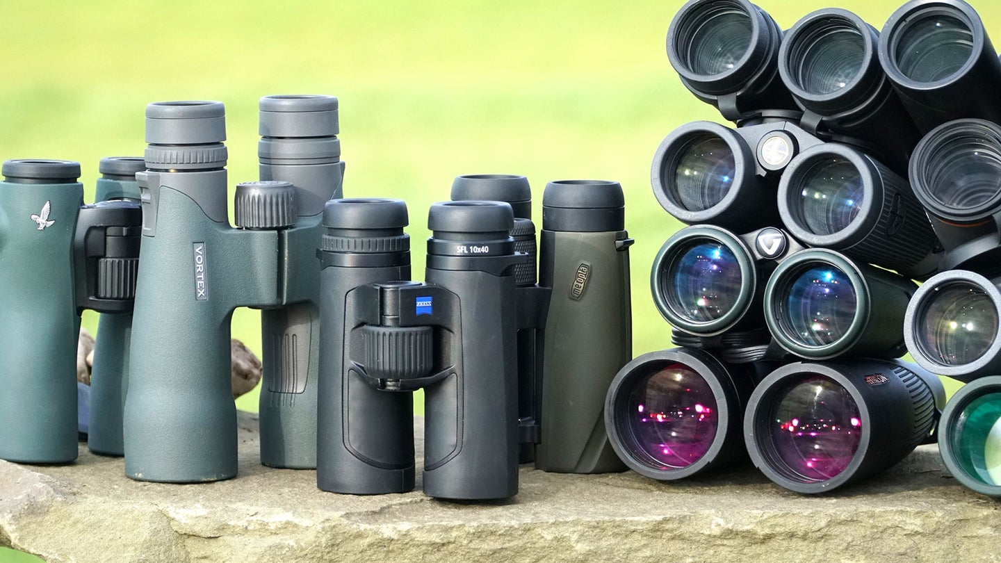 Large group of binoculars sitting on field stone with green field in background