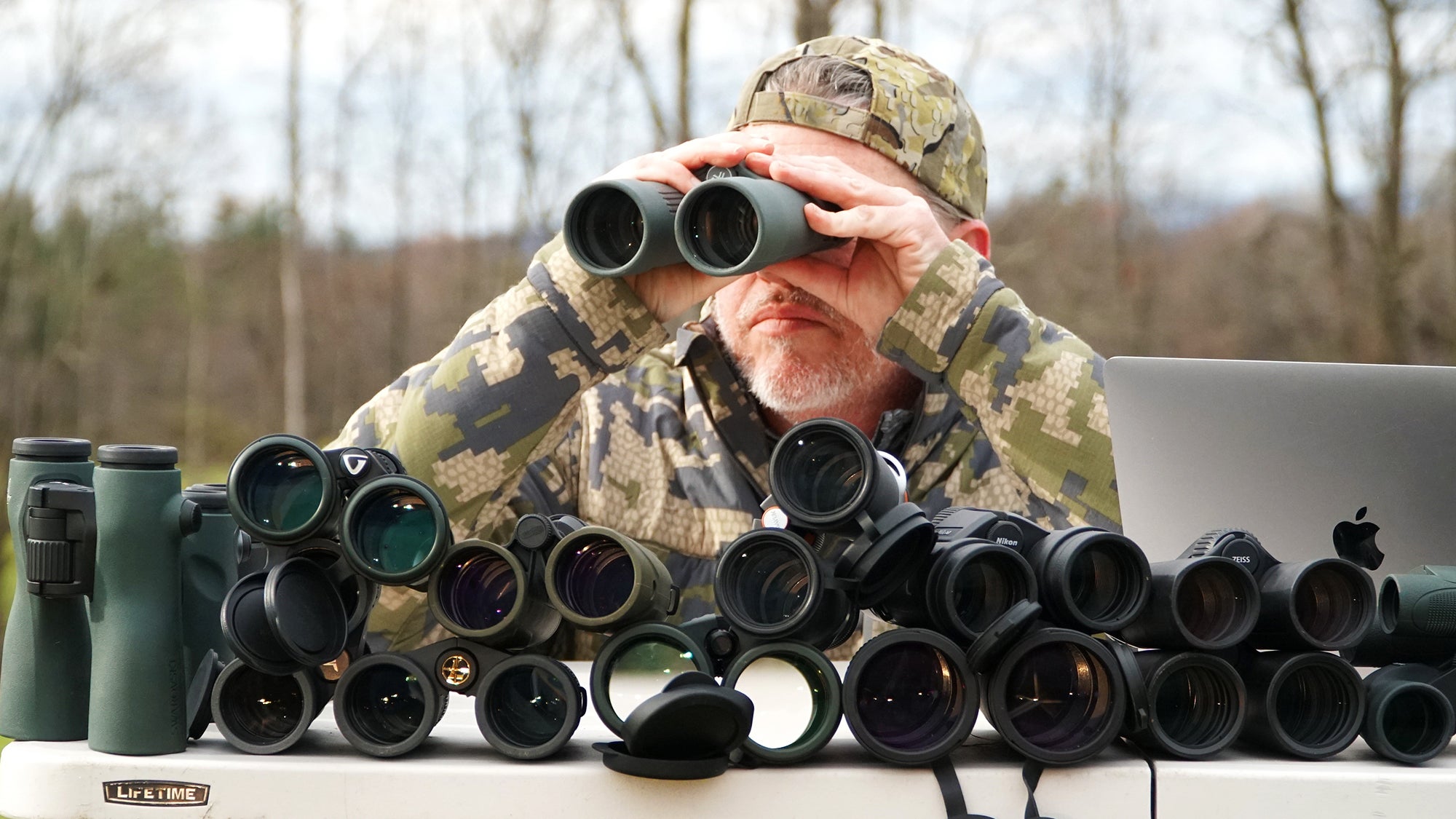 The author tests a pair of binoculars at a table laden with other binoculars