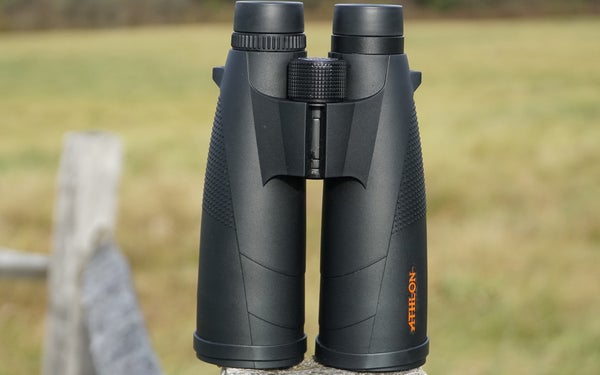 Athlon Cronus 15x56 binocular sitting on a fence post with field in background.