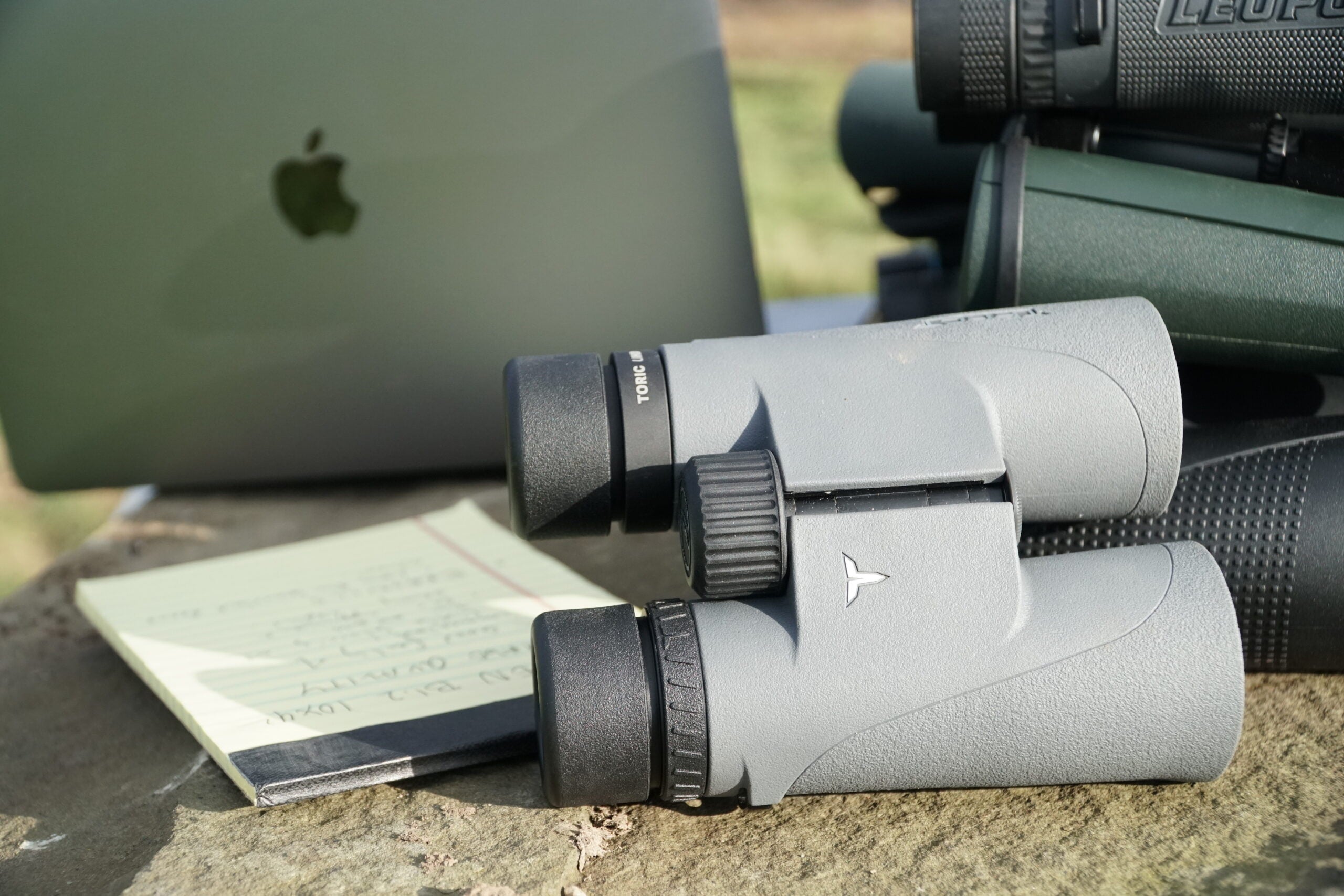 Tract Toric UHD 10x42 binocular sitting on talbe with computer and note pad.