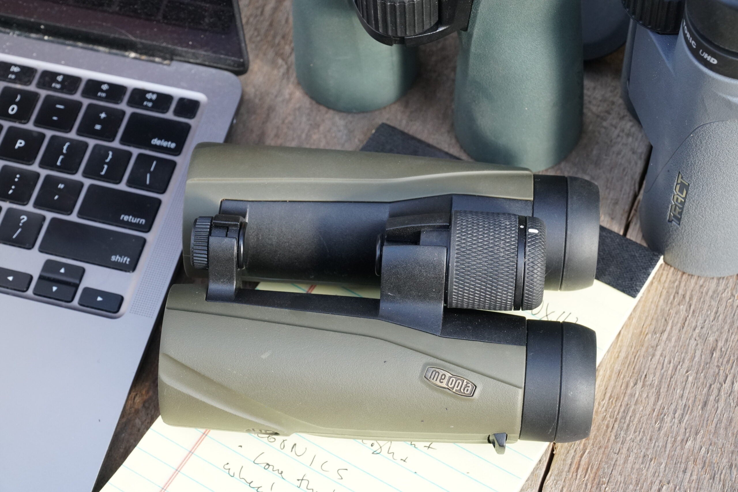 Meopta binocular lying on a table with a notepad, computer, and other binoculars.