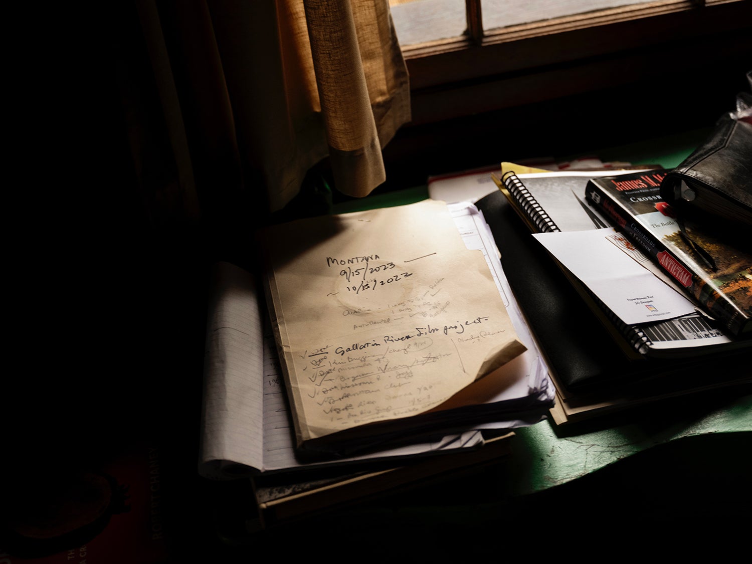 A collection of books and papers rests on a desk inside a dark cabin.