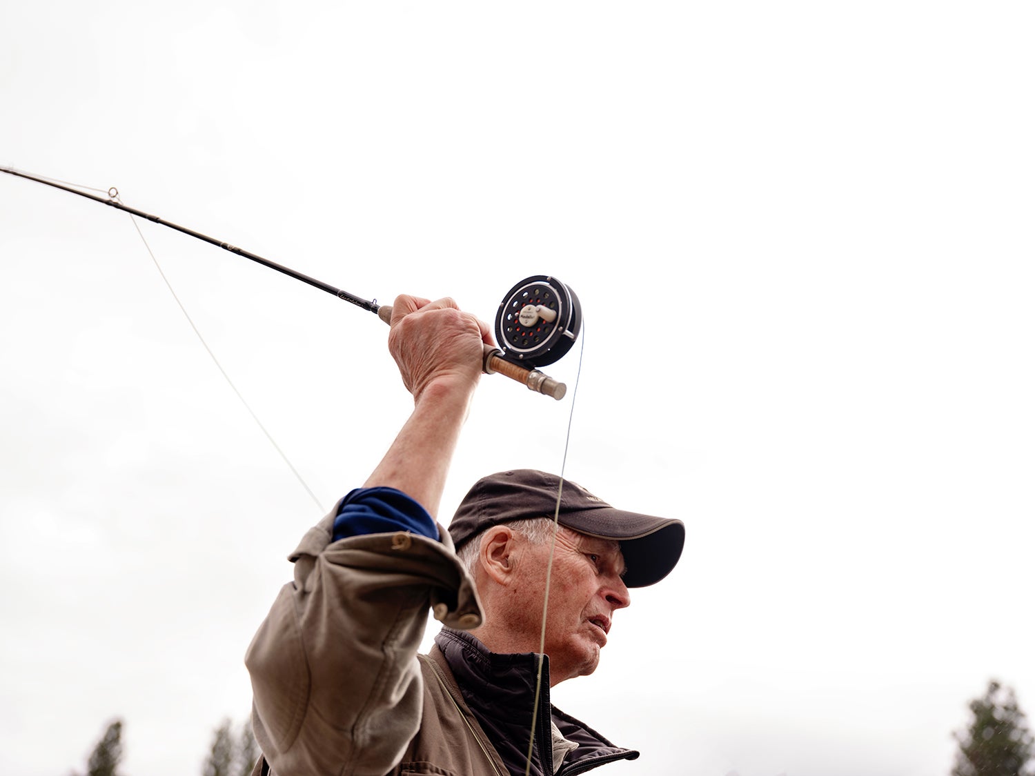 A man wearing a brown hat and vest casts a fly fishing rod in Montana.