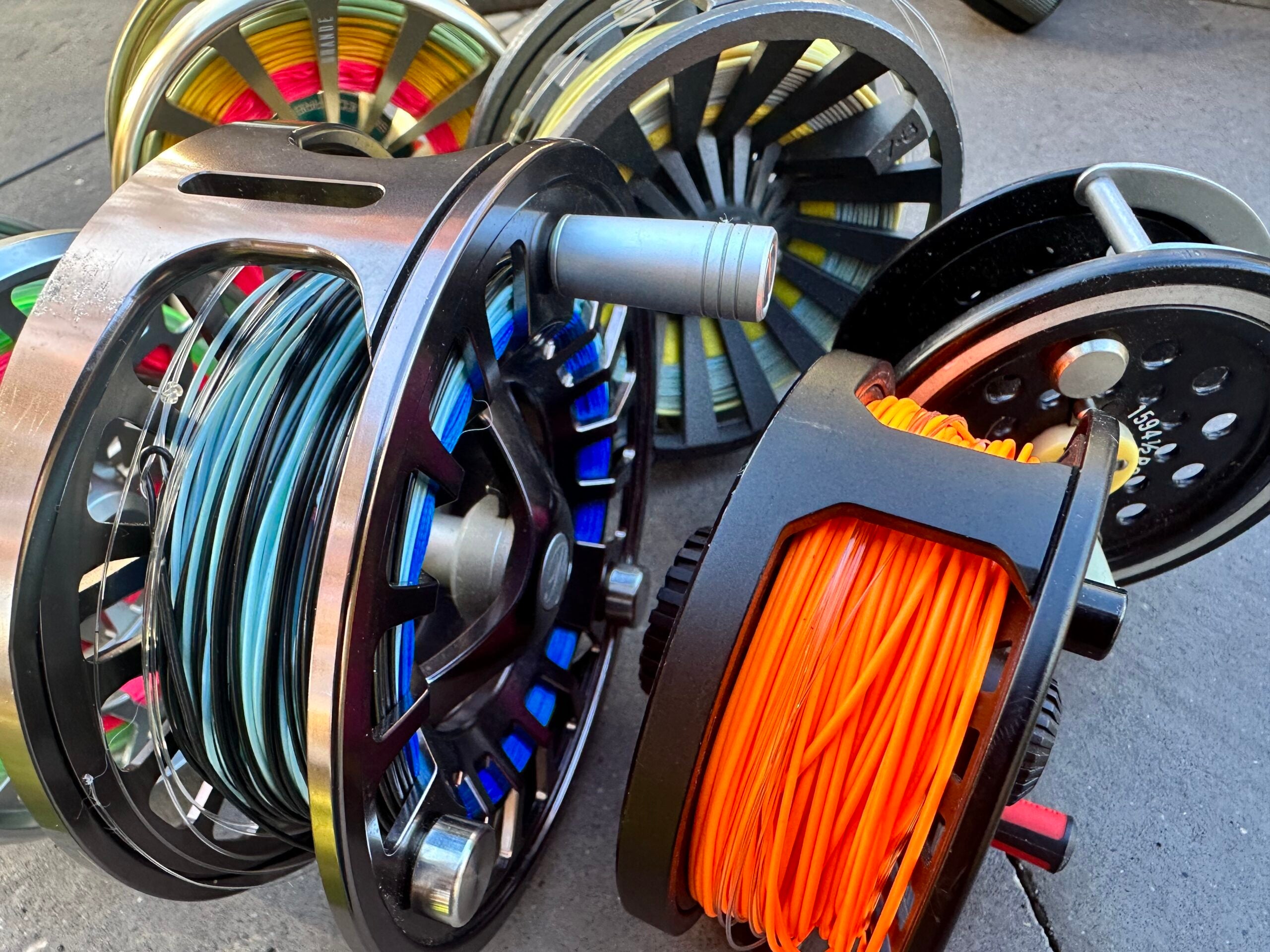 Five fly fishing reels with brightly colored fly lines are arranged on a table.