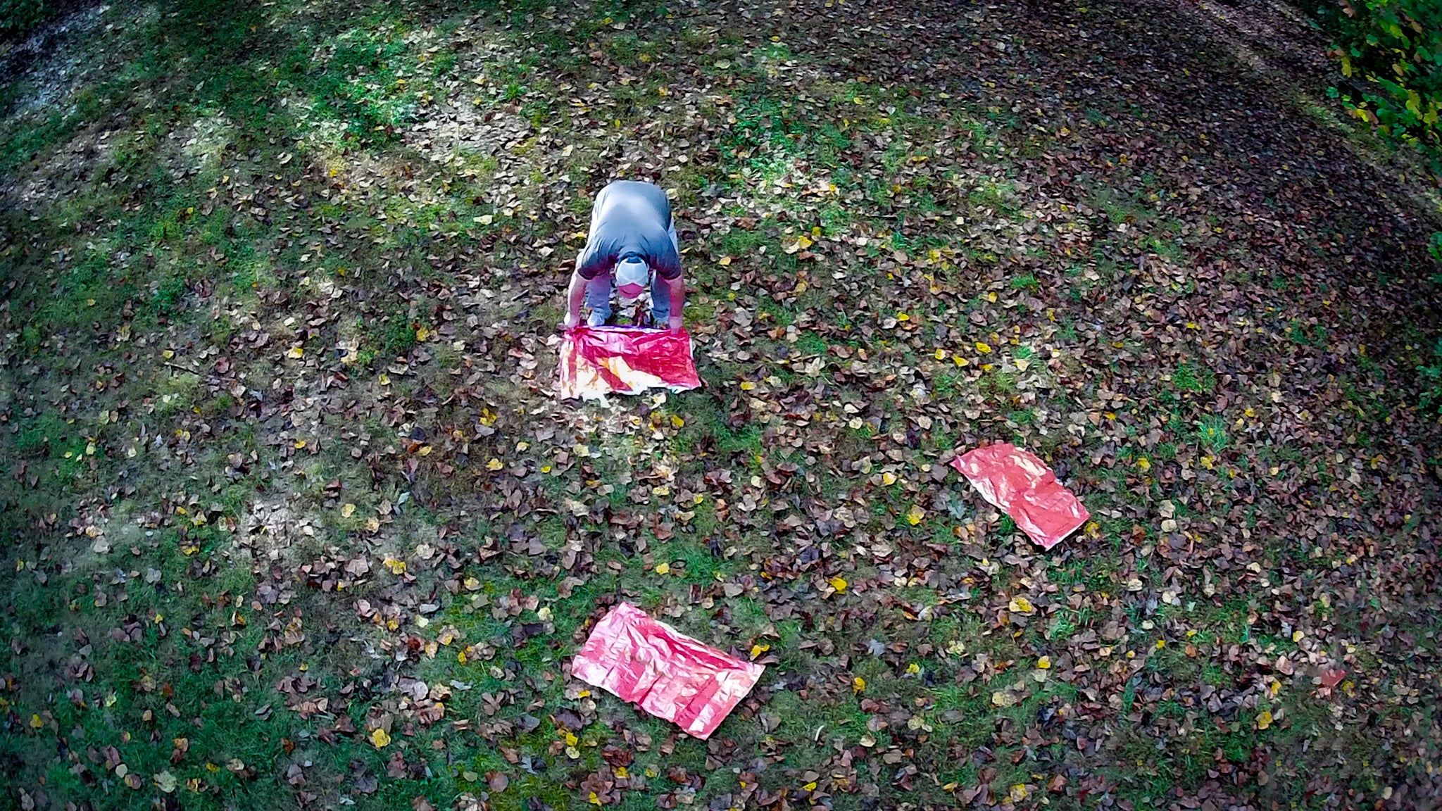 A man lays red emergency blankets on the ground to attract the attention of search teams from above.