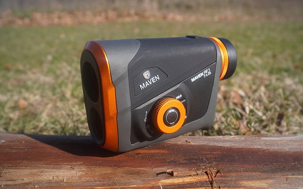 The orange and gray Maven RF.1 rangefinder sitting on a brown log in a lawn.