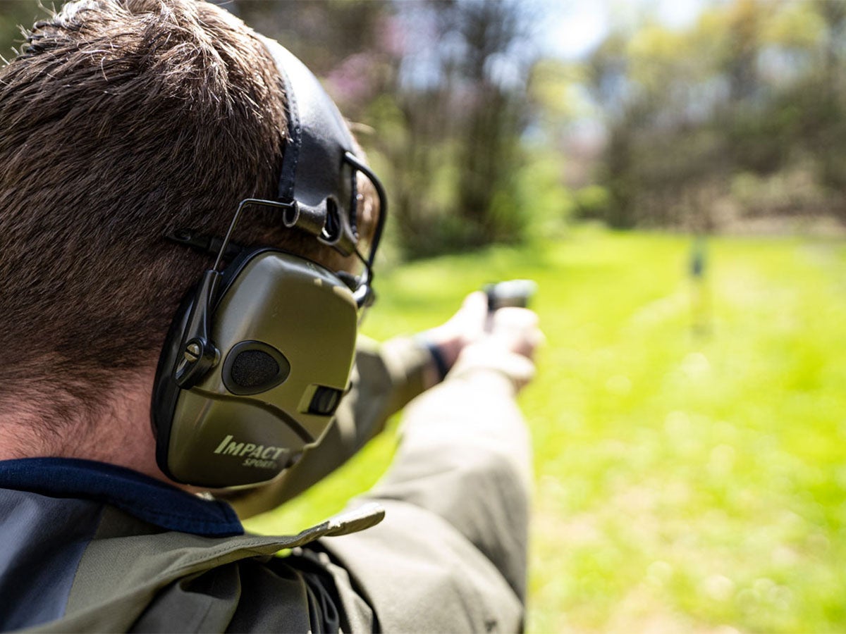 A man wearing IMpact Sport hearing protection while shooting a pistol at a range