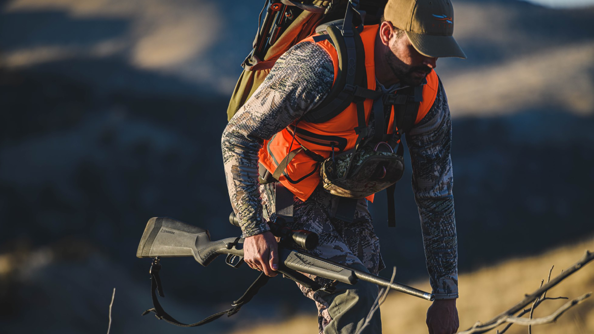 Hunter wearing orange vest carrying rifle up hill