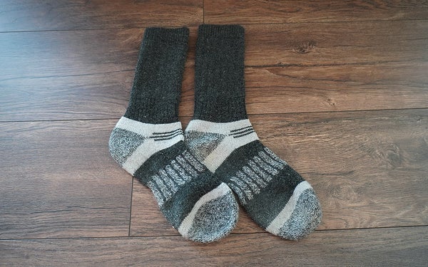 A pair of Magellan Outdoors Repreve hunting socks sitting on a dark wooden floor.