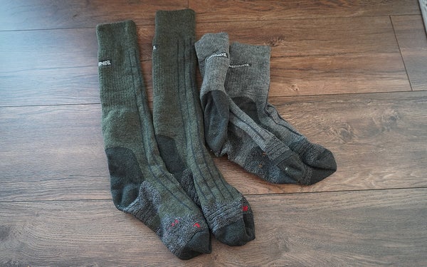 Two pairs of Meindl socks in grey and green sitting on a hardwood floor.