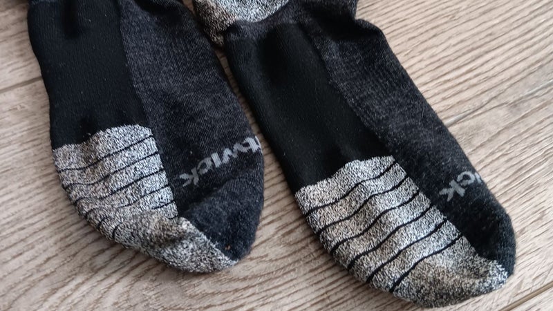The bottom of a pair of black and gray Swiftwick trail socks on a hardwood floor. 