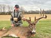 Hunter Loga Patterson kneels in a field, showing off a huge whitetail buck