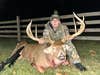 Hunter Tanner Eggelton sits on the ground near a fence, showing off a huge whitetail buck