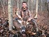 Hunter sits in the woods, posing with a huge whitetail buck