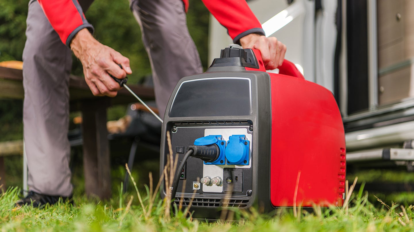 A man pulls the cord to start a gas-powered inverter generator on a lawn