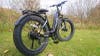 A black Aventon Aventure.2 electric fat tire bike sitting on a grassy lawn in front of a metal gate. 