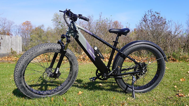 A grey, purple, and black Lectric X-Peak electric bike in a grassy backyard. 