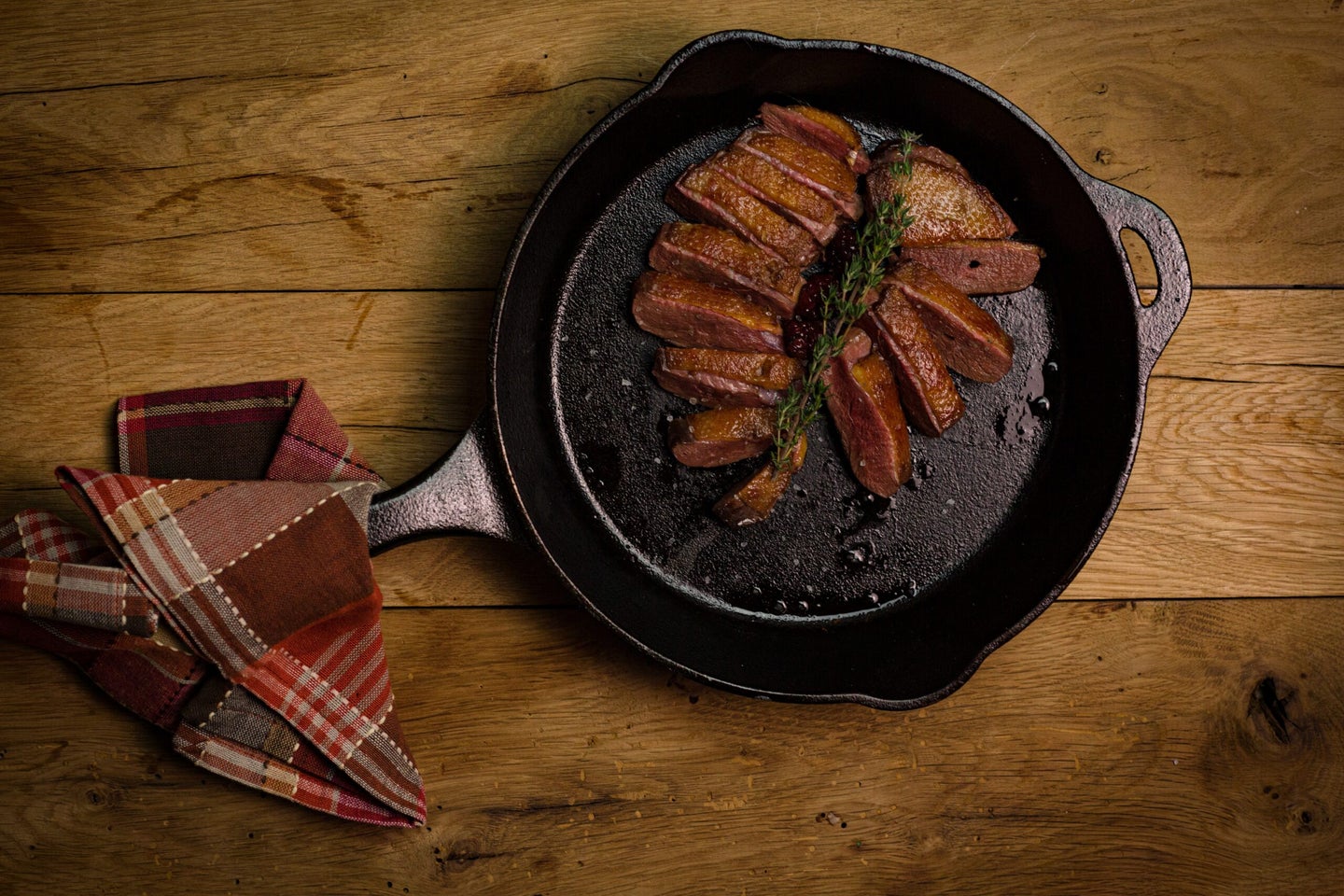 Sliced duck breast in a black cast iron skillet resting on a wooden table.
