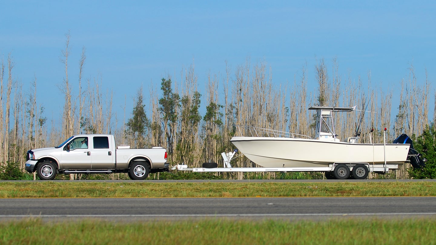 A white pickup truck towing a white boat down the highway
