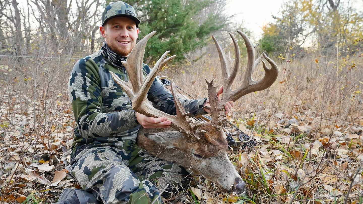 Kansas hunter sitting in a leafy opening posing with a huge whitetail buck taken with a bow