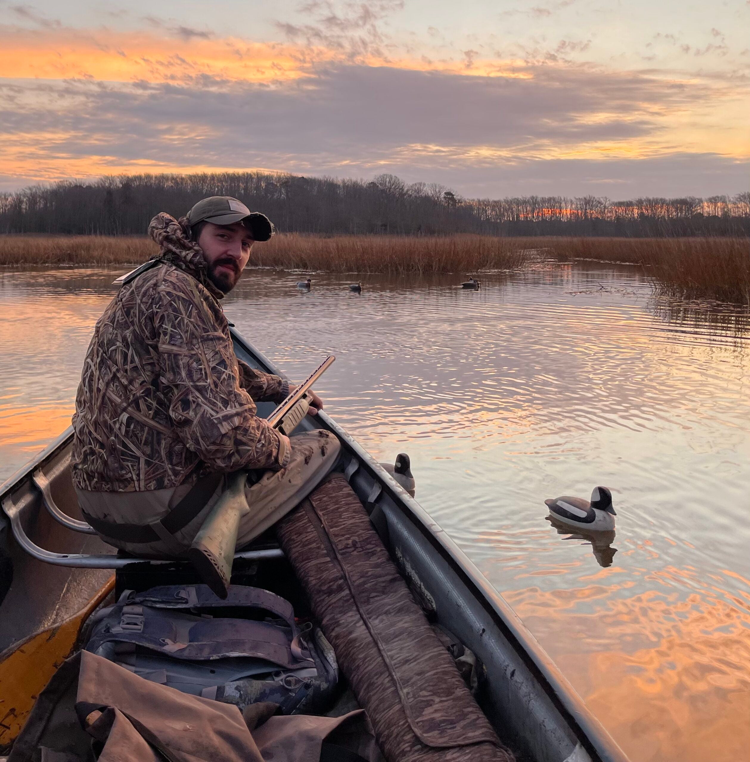 Man hunting waterfowl on a pond from a canoe with duck decoys nearby
