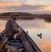 Man hunting waterfowl on a pond from a canoe with duck decoys nearby