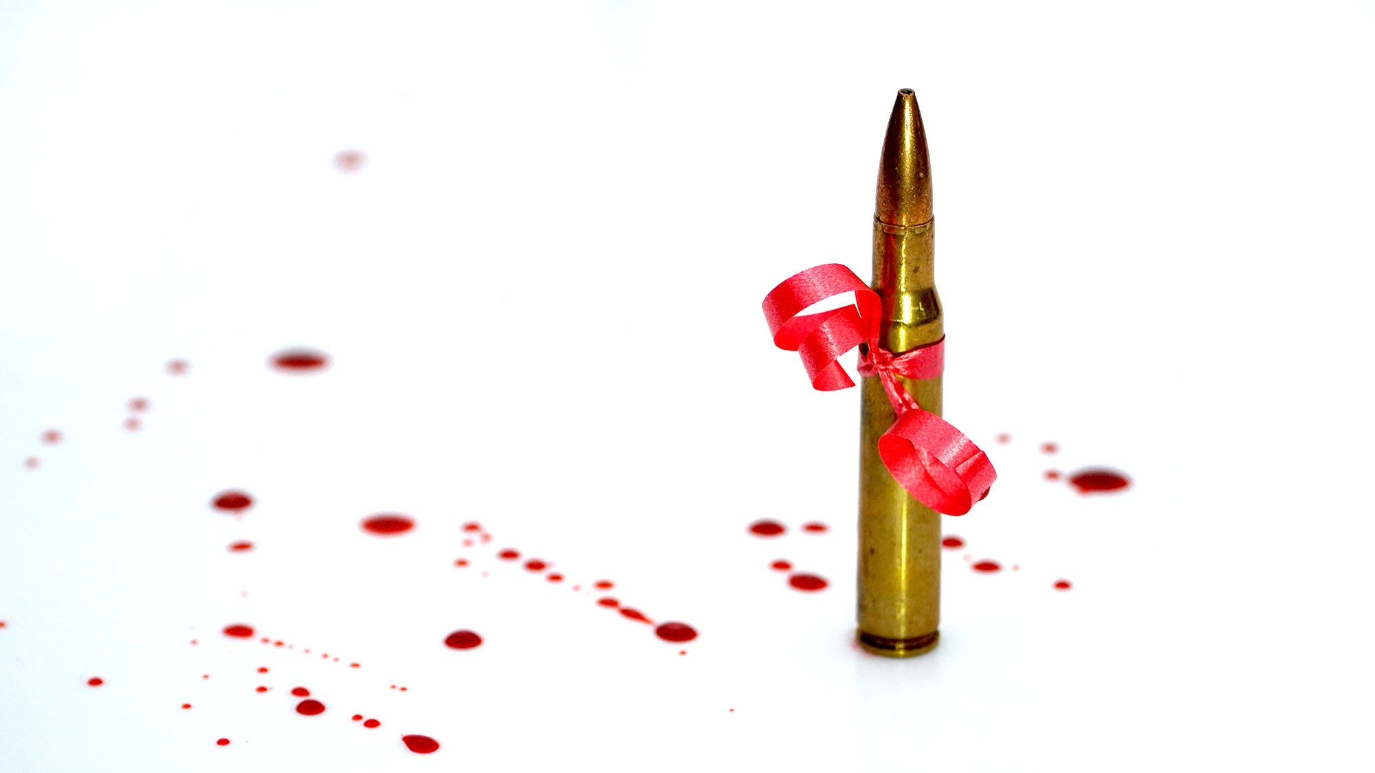 A 30-06 bullet with a red ribbon and spots of blood on a white background