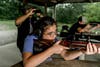 A girl fires a rifle at a gun range, with adults overseeing and ensuring the rules of gun safety