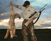 A hunter with a rifle in one hand hold up a coyote in the other