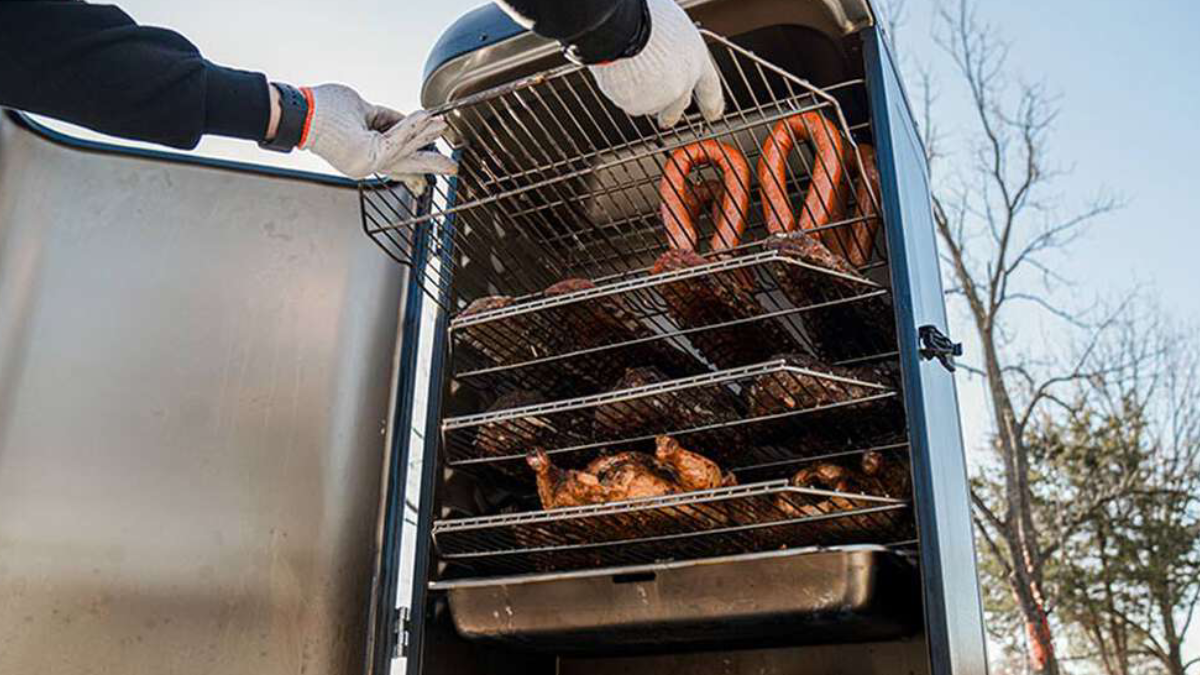 Man loading chicken and sausage into Grilla Mammoth Vertical Smoker