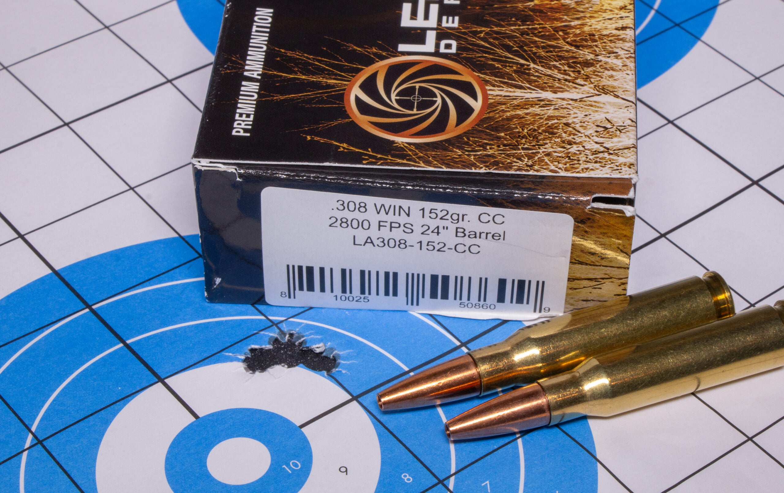 A rifle target with several bullet holes with a box of 308 ammo and two loose cartridges