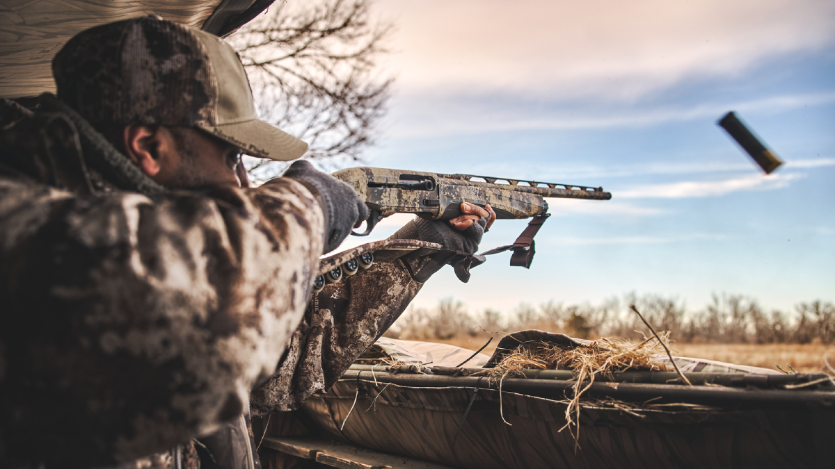 Hunter shooting shotgun in duck blind